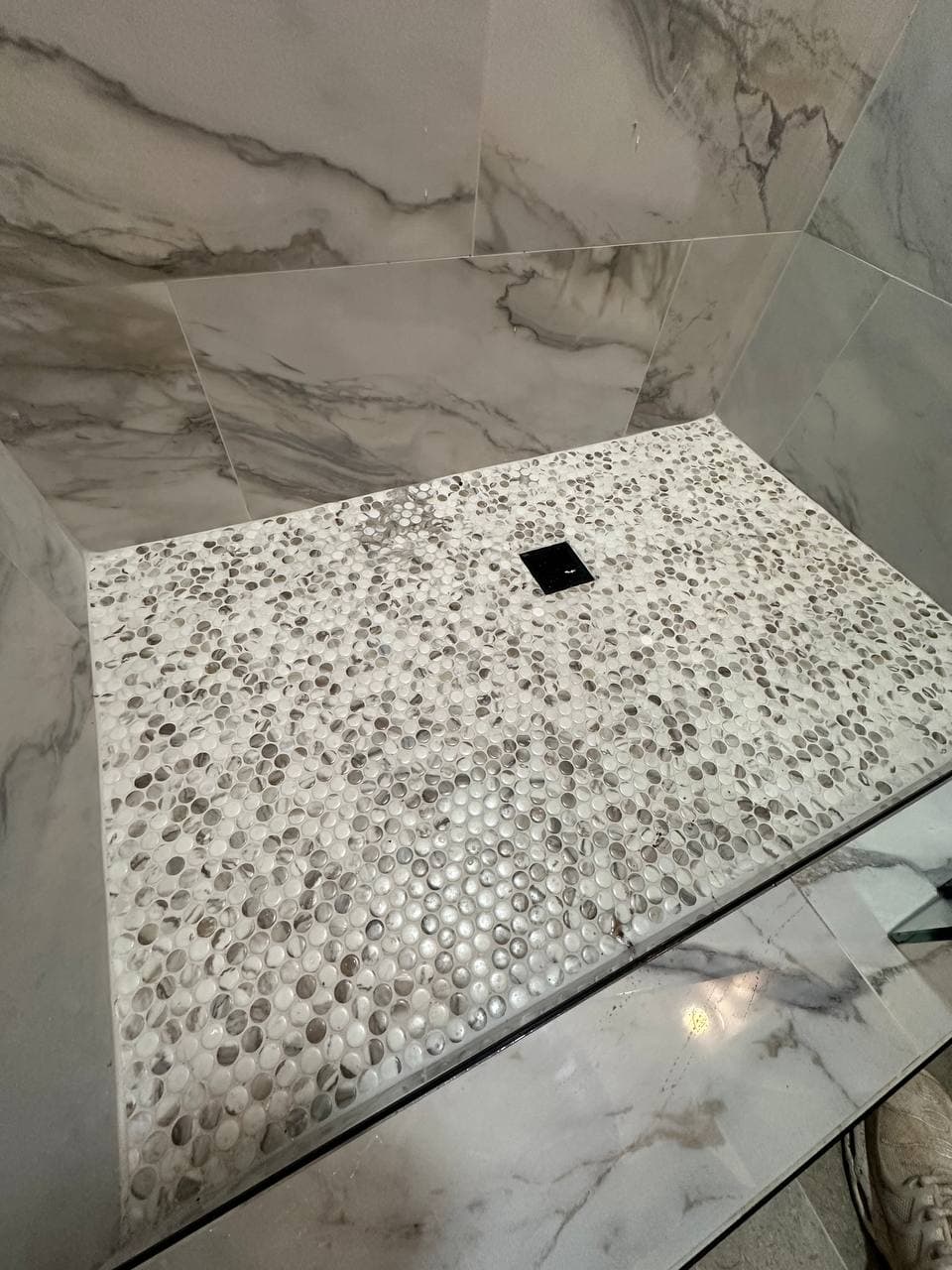 Marble tile shower with frameless glass door and black vanity